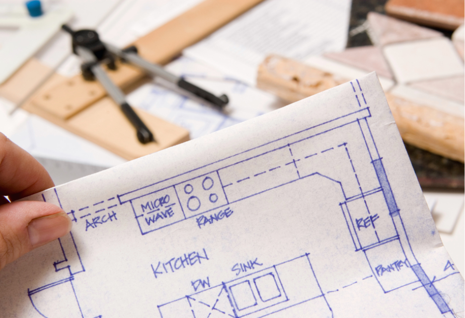 Hand holding a kitchen floor plan showing the layout of appliances, sink, refrigerator, pantry, and kitchen work areas.